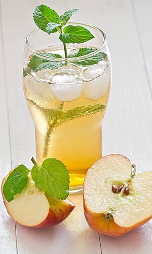 Apple spritzer with apple slices on a white wooden tray with a green background.
